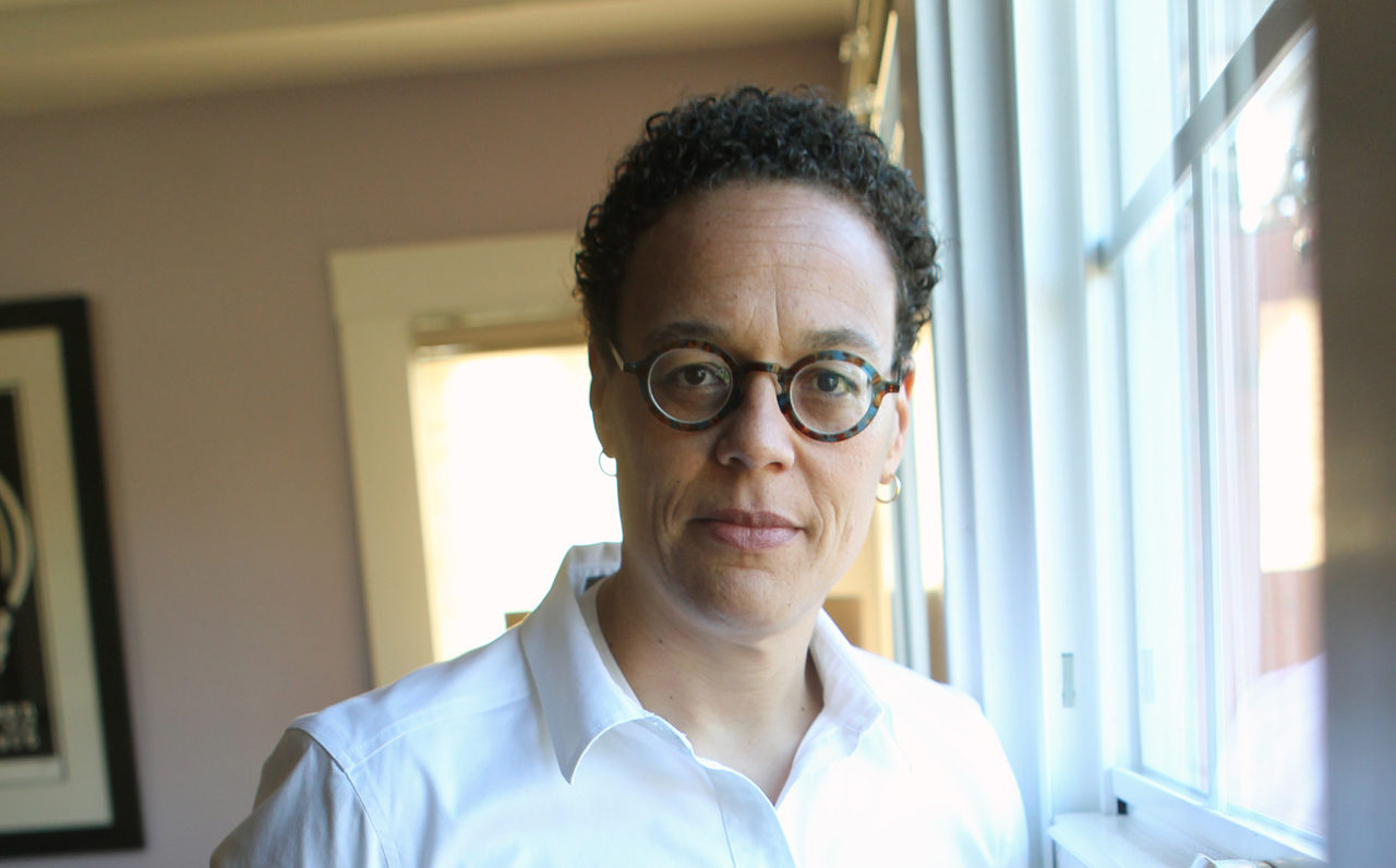 a black woman in glasses and a white shirt with a determined expression